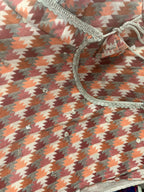 Patterned fabric with a houndstooth design in brown, orange, and beige tones.